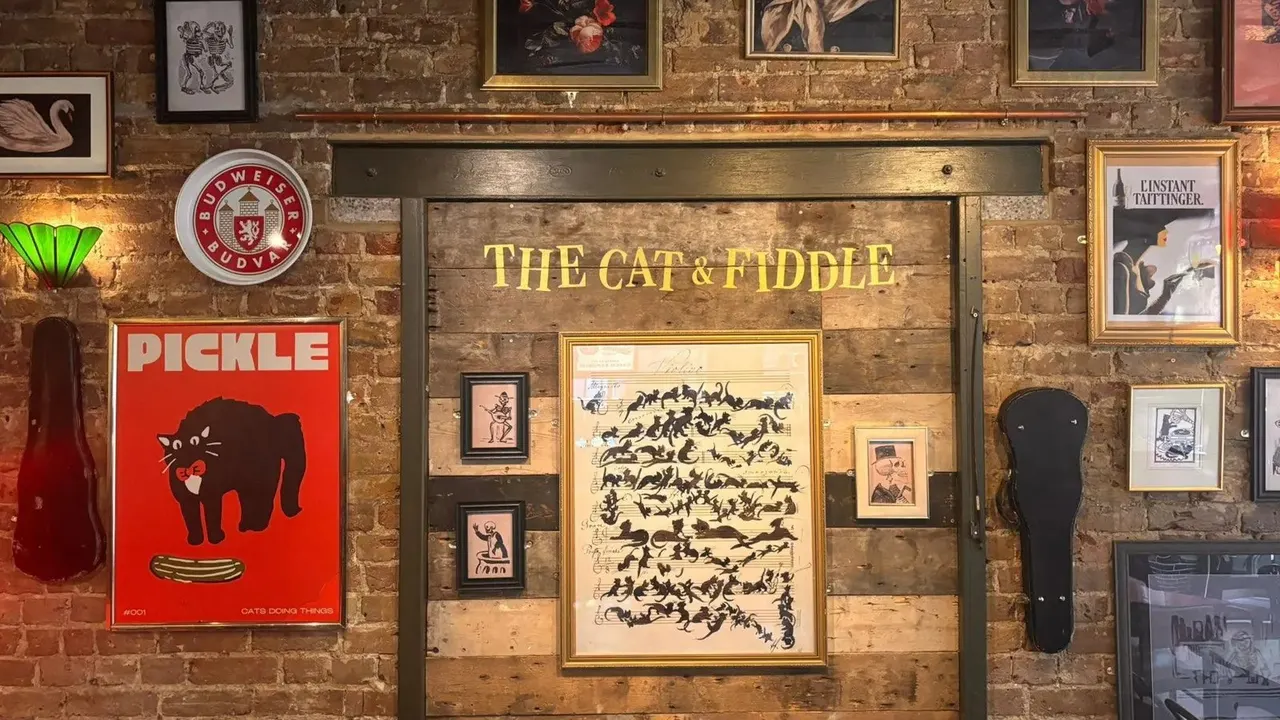 The brick feature wall at Cat & Fiddle, with its name in lights, framed prints and a red Pickle poster
