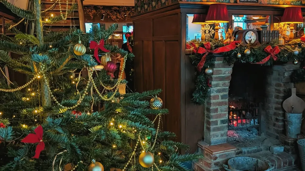 A Christmas tree with gold baubles and fairy lights beside a lit brick fireplace hung with garland and red bows at The Pullman, Folkestone
