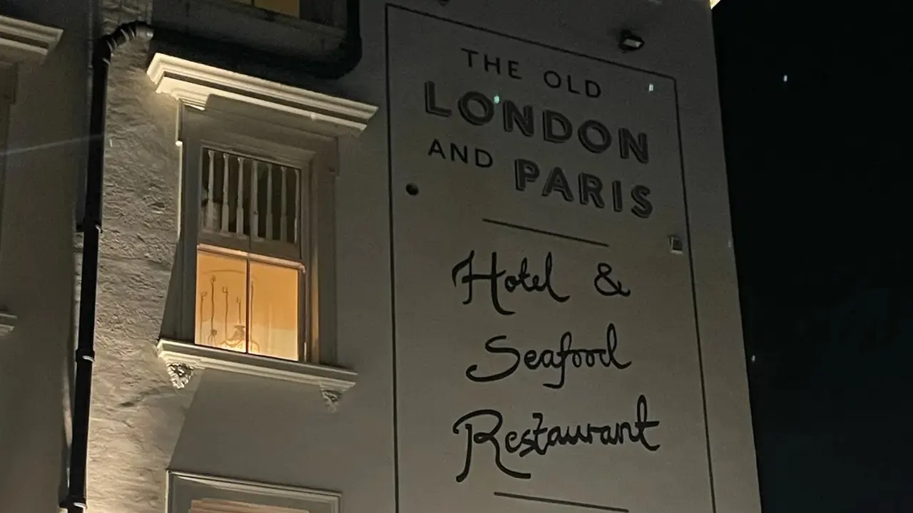 The front of London & Paris Hotel on Harbour Street at night, its painted sign lit up