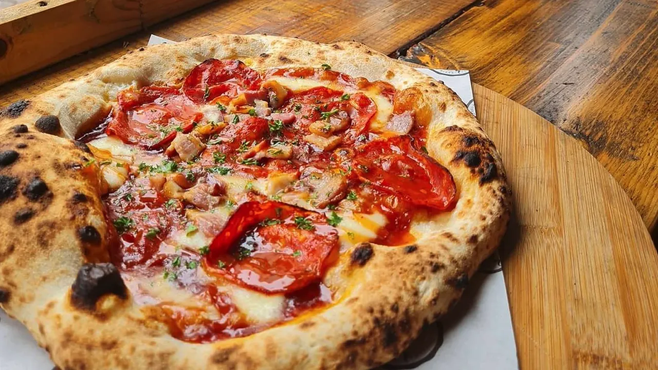 A wood-fired pepperoni pizza with a charred, puffy crust on a wooden board by the window at Luben