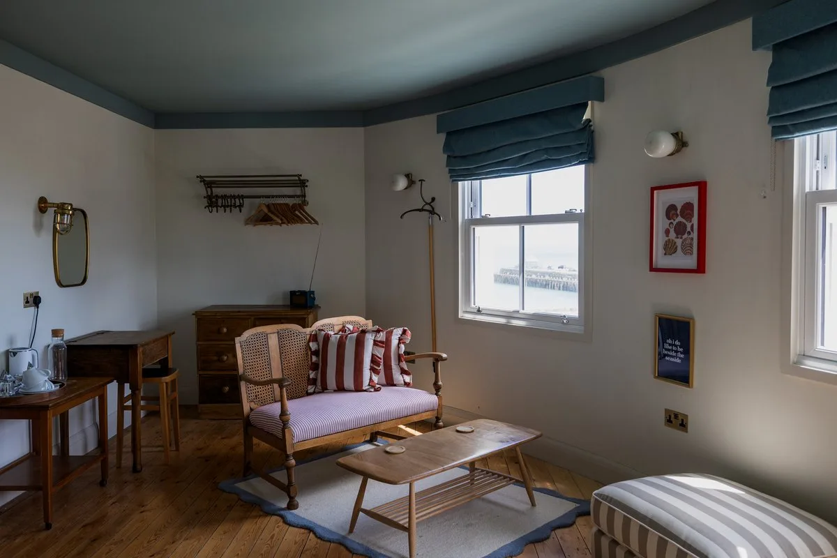 A bedroom sitting area at London & Paris Hotel with a cane sofa, striped cushions and a tall window