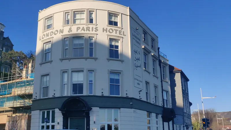 The curved white frontage of London & Paris Hotel on Harbour Street, its name in raised letters, under a deep blue sky