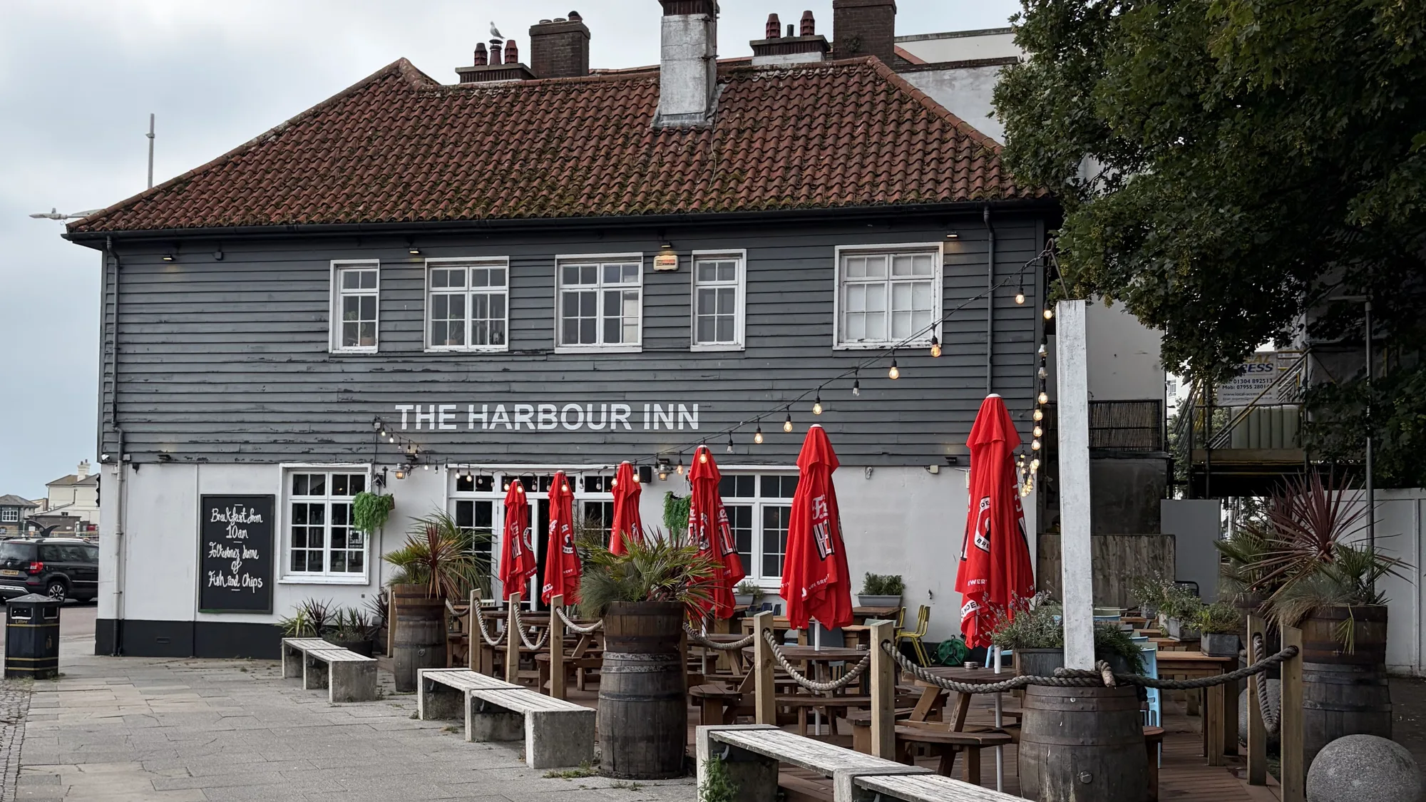 Harbour Inn’s grey weatherboarded front on Harbour Street, with its name in white letters and the terrace laid out with benches and red parasols