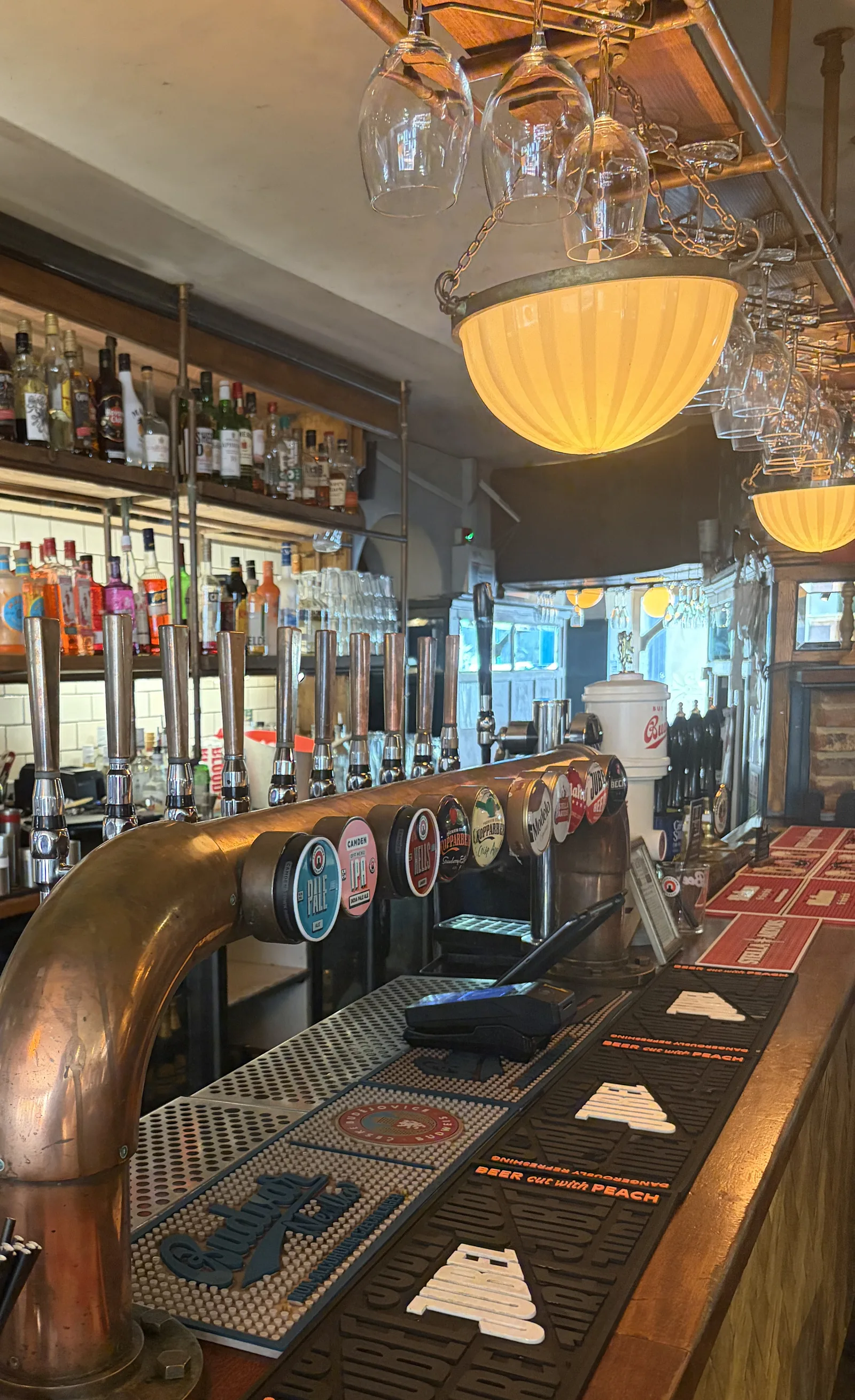 The bar at The Pullman: brass beer taps, hanging glasses and a glowing glass lamp, with shelves of spirits behind