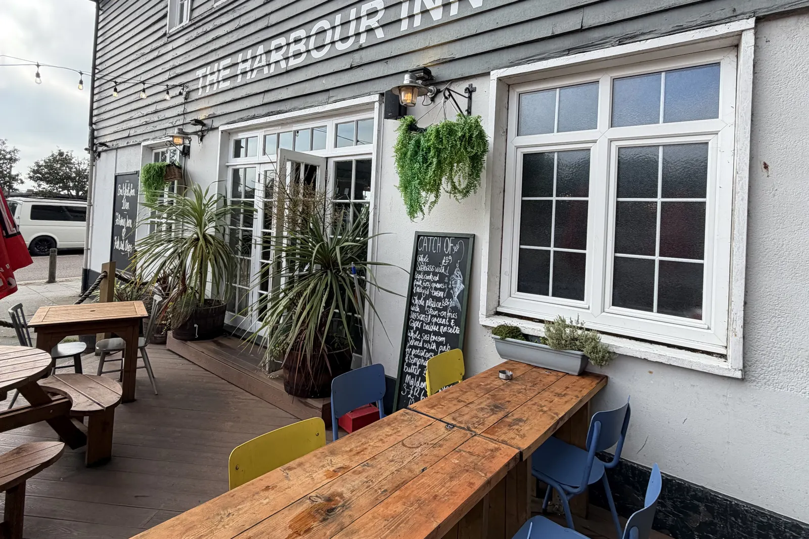 The side terrace at Harbour Inn, Folkestone, with wooden tables, planters and blue chairs