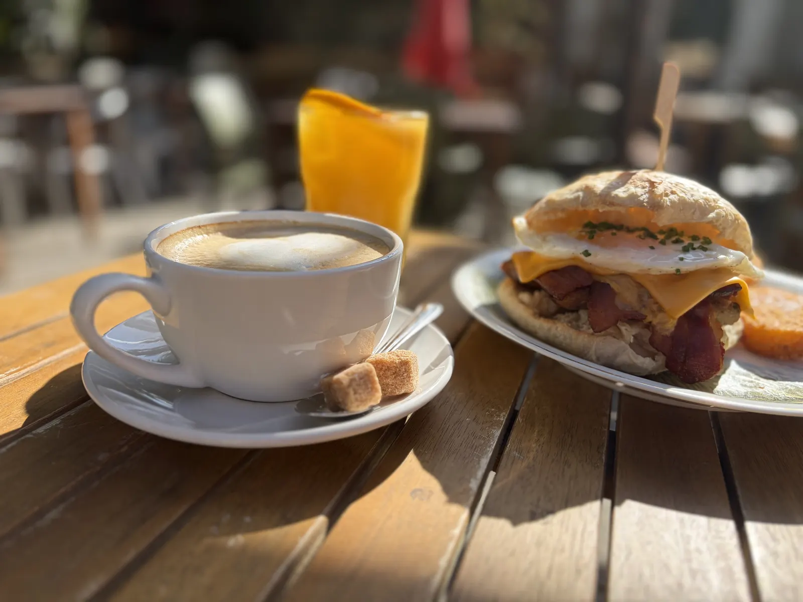 A cappuccino, a glass of orange juice and a breakfast roll with egg, bacon and cheese on a sunny garden table at The Pullman, Folkestone