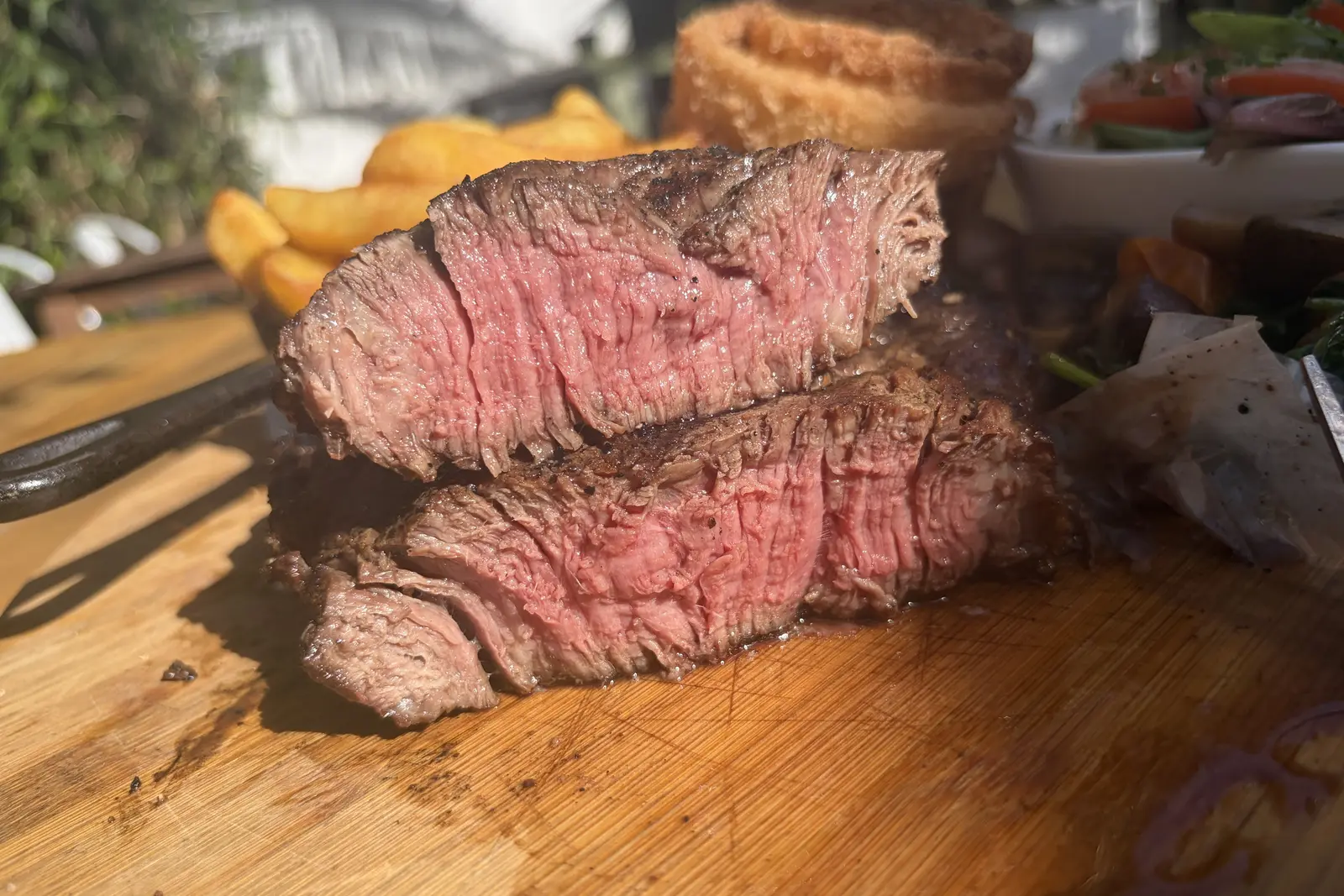 Sliced pink steak on a wooden board with chips and onion rings at The Pullman, Folkestone