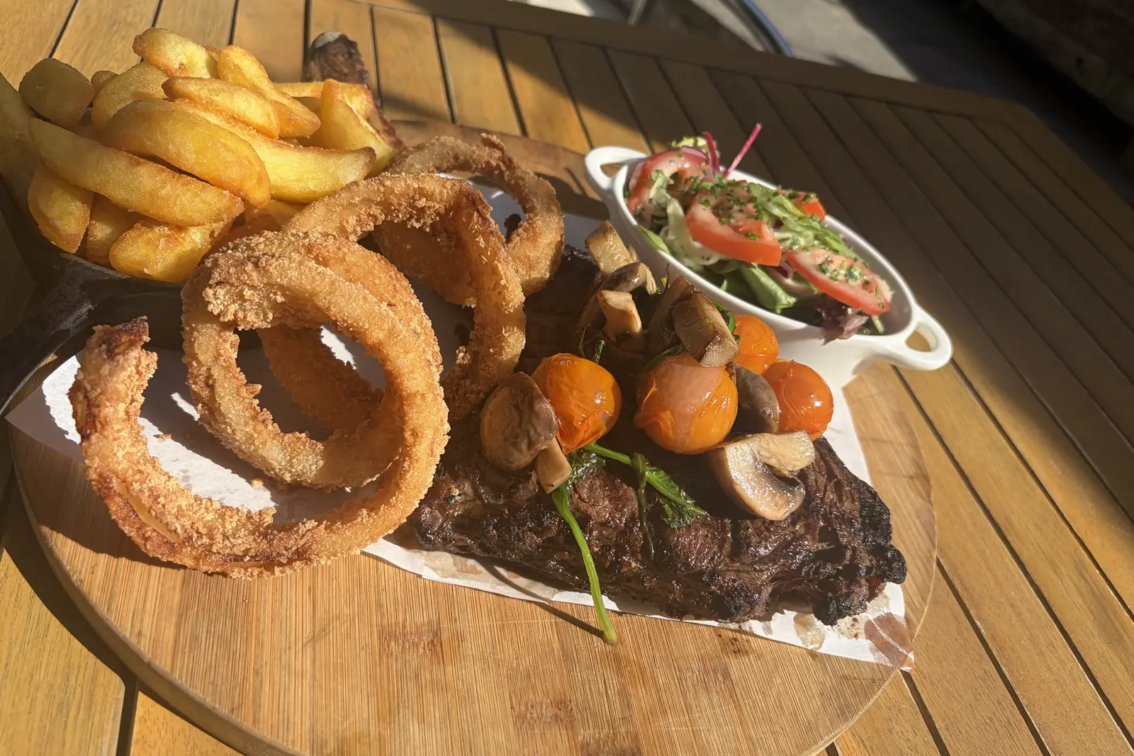 A steak sharing board with chips, onion rings and salad on a sunny garden table at The Pullman, Folkestone