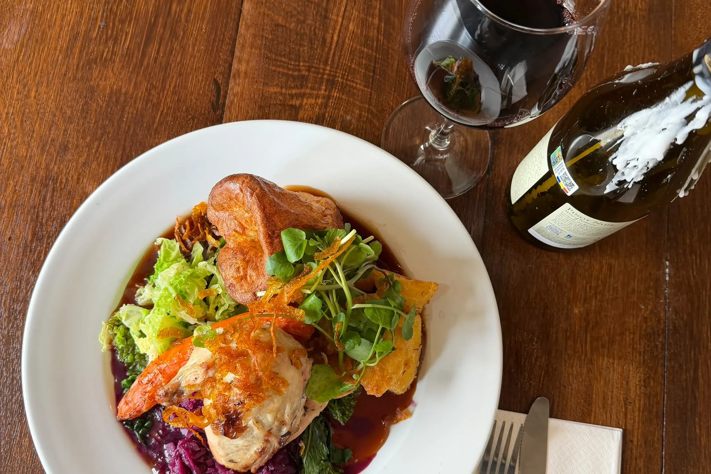 A roast chicken plate and a glass of red wine on a wooden table at The Ship Inn, Sandgate