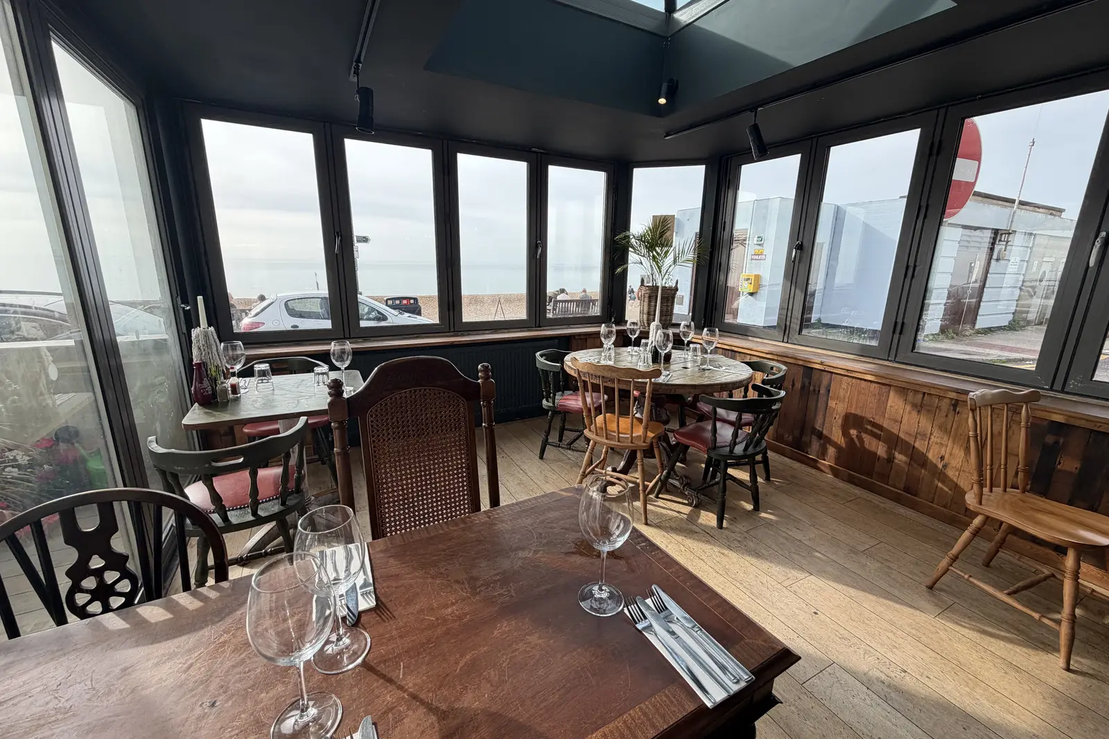 The glazed sea-view dining room at The Ship Inn, Sandgate, with round tables and wooden chairs